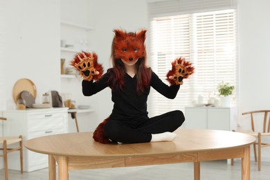 Photo of Quadrobics. Girl wearing fox mask, tail and gloves on table at home