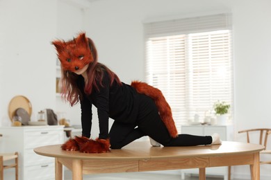 Photo of Quadrobics. Girl wearing fox mask, tail and gloves on table at home