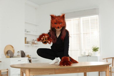 Photo of Quadrobics. Girl wearing fox mask, tail and gloves on table at home