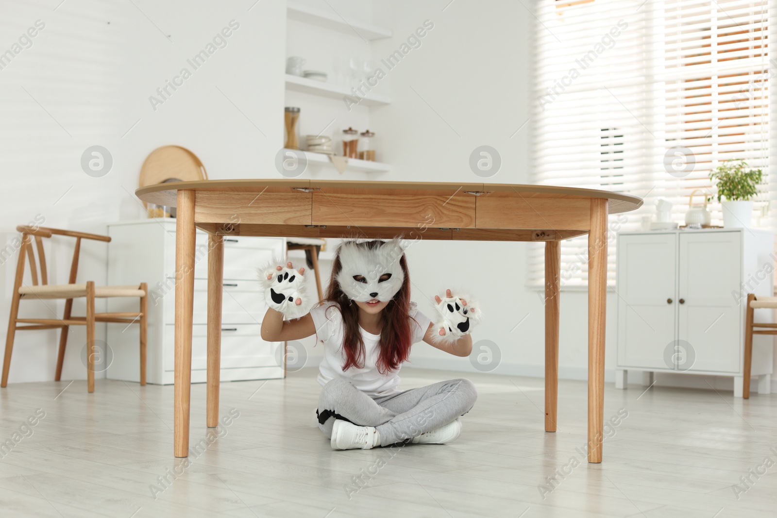 Photo of Quadrobics. Girl wearing cat mask and gloves under table at home