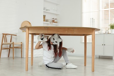 Photo of Quadrobics. Girl wearing cat mask, tail and gloves under table at home