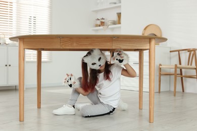 Photo of Quadrobics. Girl wearing cat mask, tail and gloves under table at home