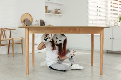 Photo of Quadrobics. Girl wearing cat mask, tail and gloves under table at home