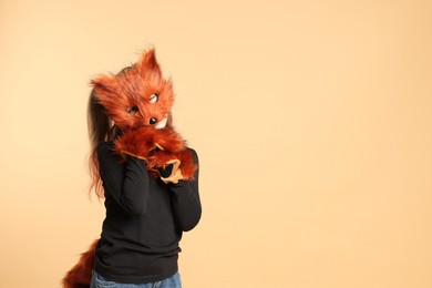 Photo of Quadrobics. Girl wearing fox mask, tail and gloves on beige background, space for text