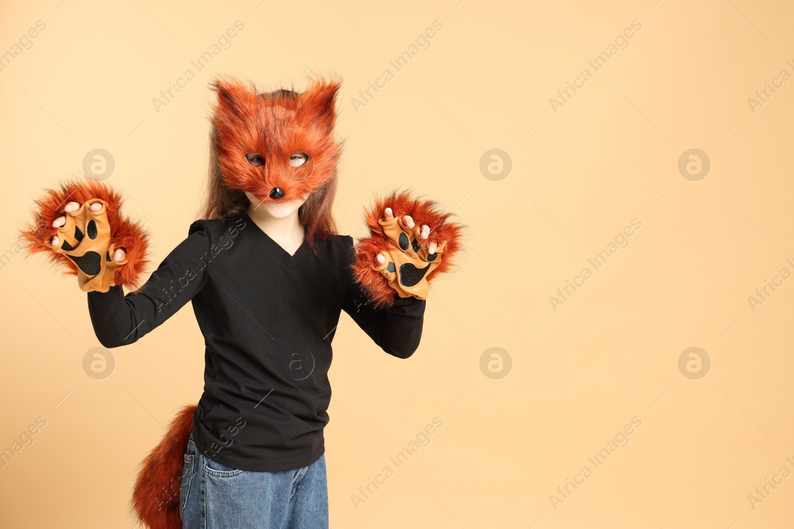 Photo of Quadrobics. Girl wearing fox mask, tail and gloves on beige background, space for text