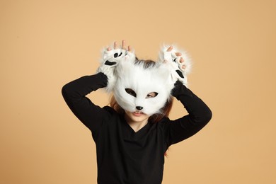 Photo of Quadrobics. Girl wearing cat mask and gloves on beige background