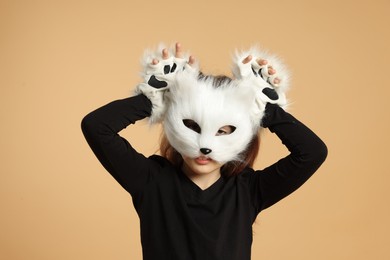 Photo of Quadrobics. Girl wearing cat mask and gloves on beige background