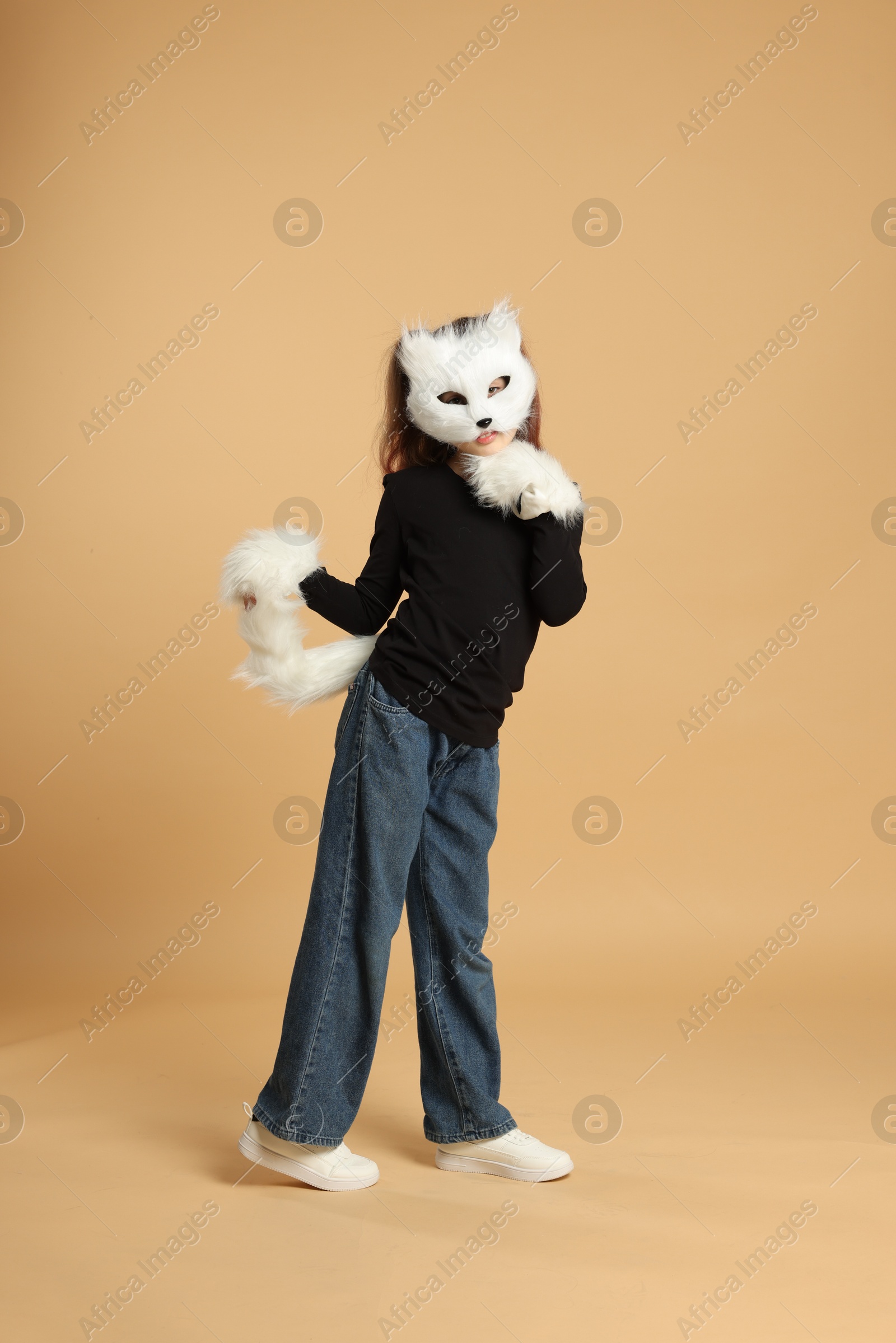 Photo of Quadrobics. Girl wearing cat mask, tail and gloves on beige background