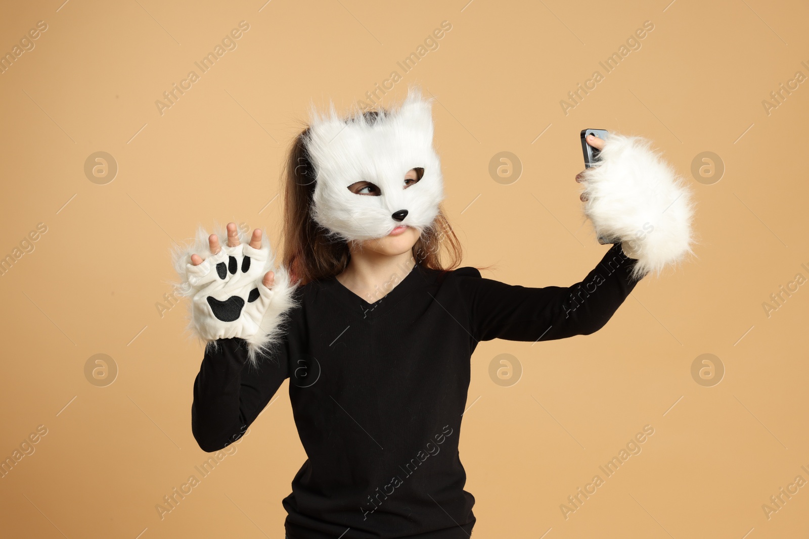 Photo of Quadrobics. Girl in cat mask and gloves taking selfie on beige background