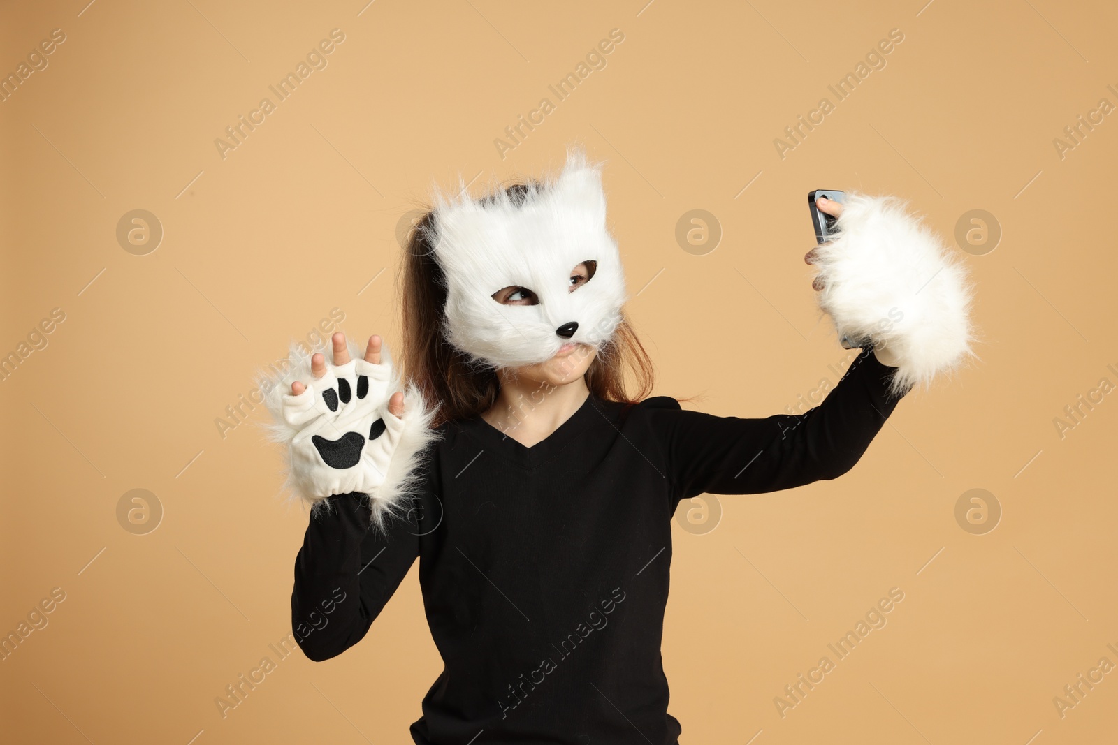 Photo of Quadrobics. Girl in cat mask and gloves taking selfie on beige background