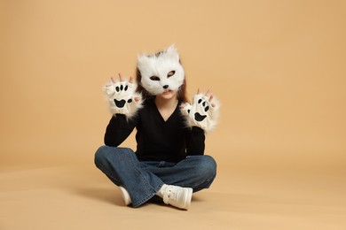 Photo of Quadrobics. Girl wearing cat mask and gloves on beige background