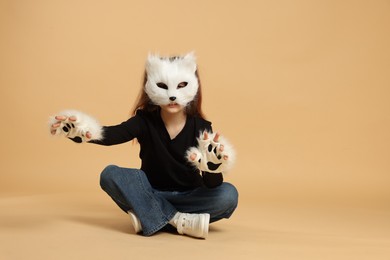 Photo of Quadrobics. Girl wearing cat mask and gloves on beige background, space for text