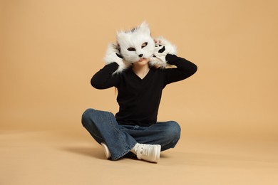 Photo of Quadrobics. Girl wearing cat mask and gloves on beige background