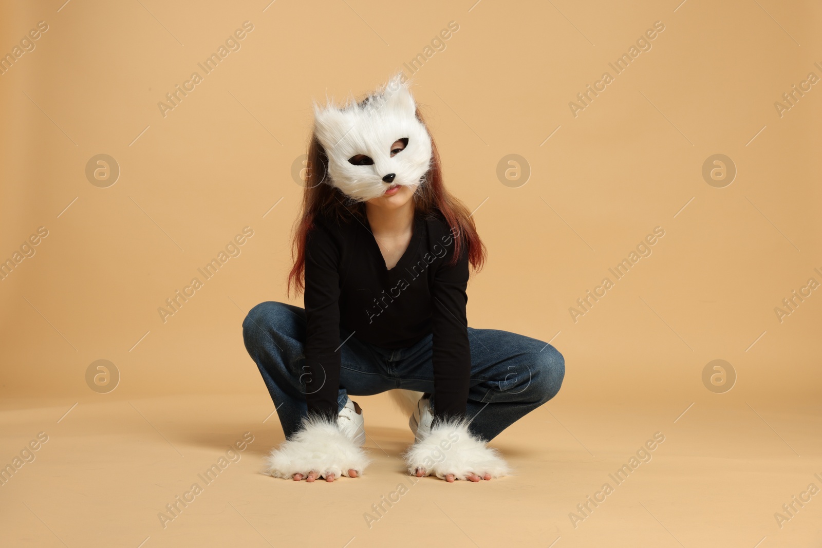 Photo of Quadrobics. Girl wearing cat mask and gloves on beige background