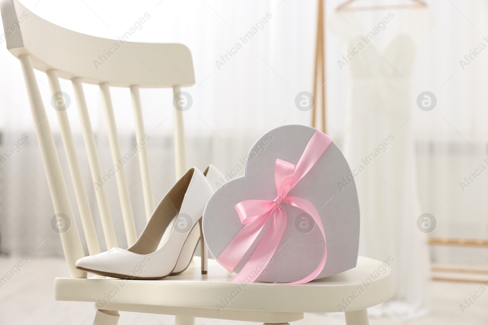 Photo of Gift box for wedding day and bridal shoes on chair indoors