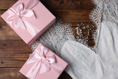 Photo of Gift boxes for wedding day, bridal dress and hair accessory on wooden background, flat lay