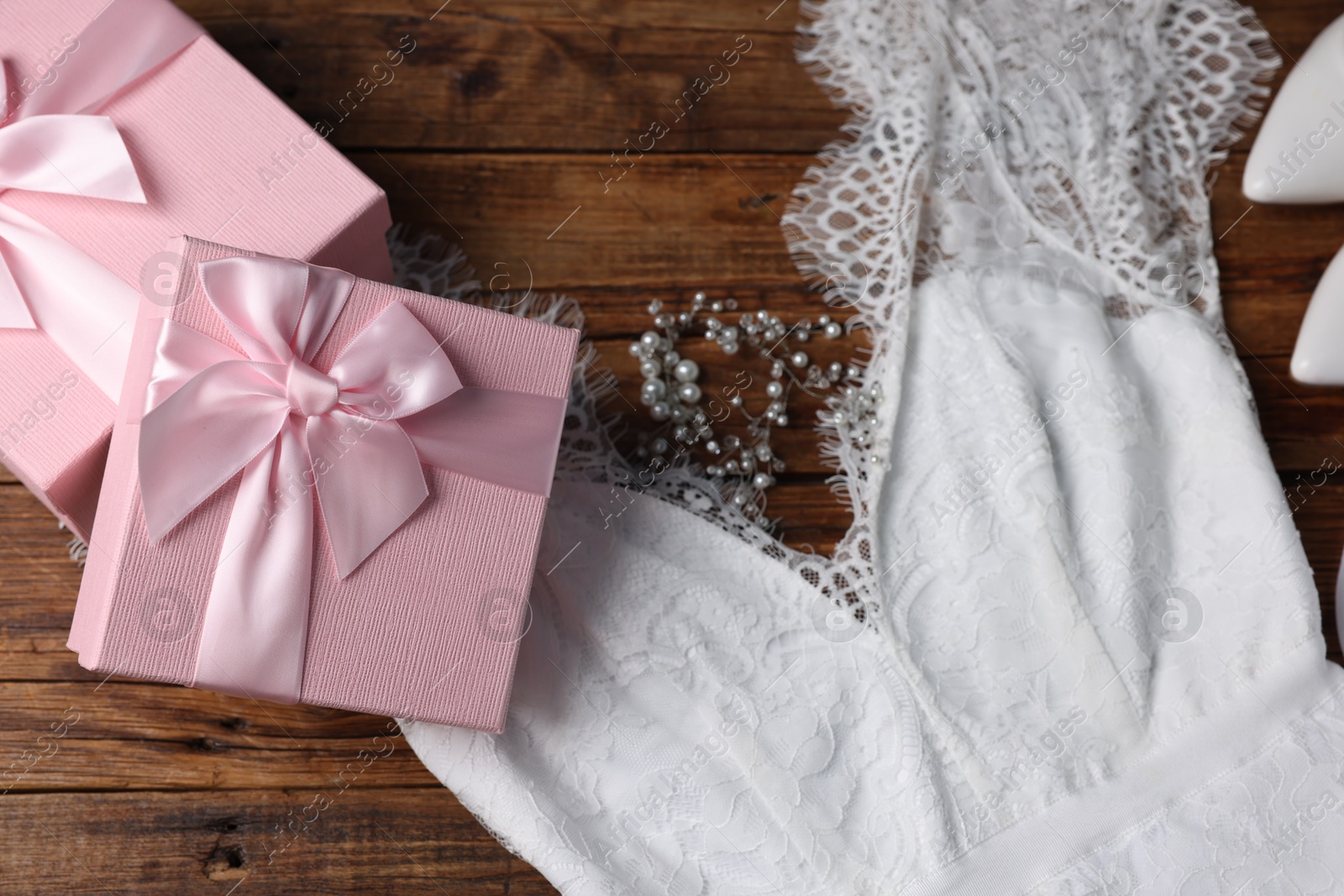 Photo of Gift boxes for wedding day and bridal dress on wooden background, flat lay