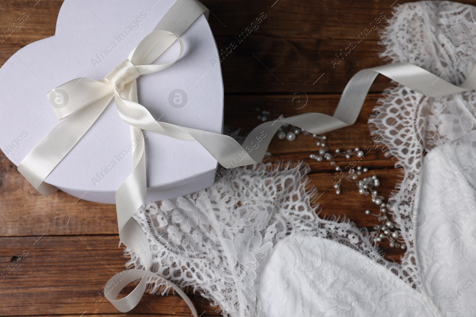 Photo of Gift box for wedding day and bridal dress on wooden background, flat lay