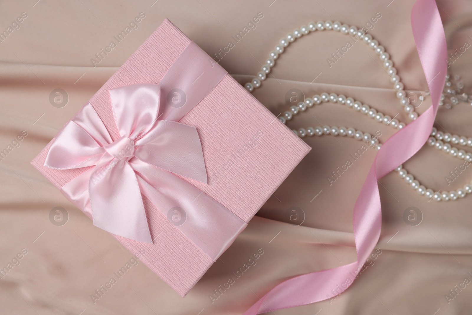 Photo of Gift box for wedding day, pearl necklace and ribbon on beige fabric, flat lay