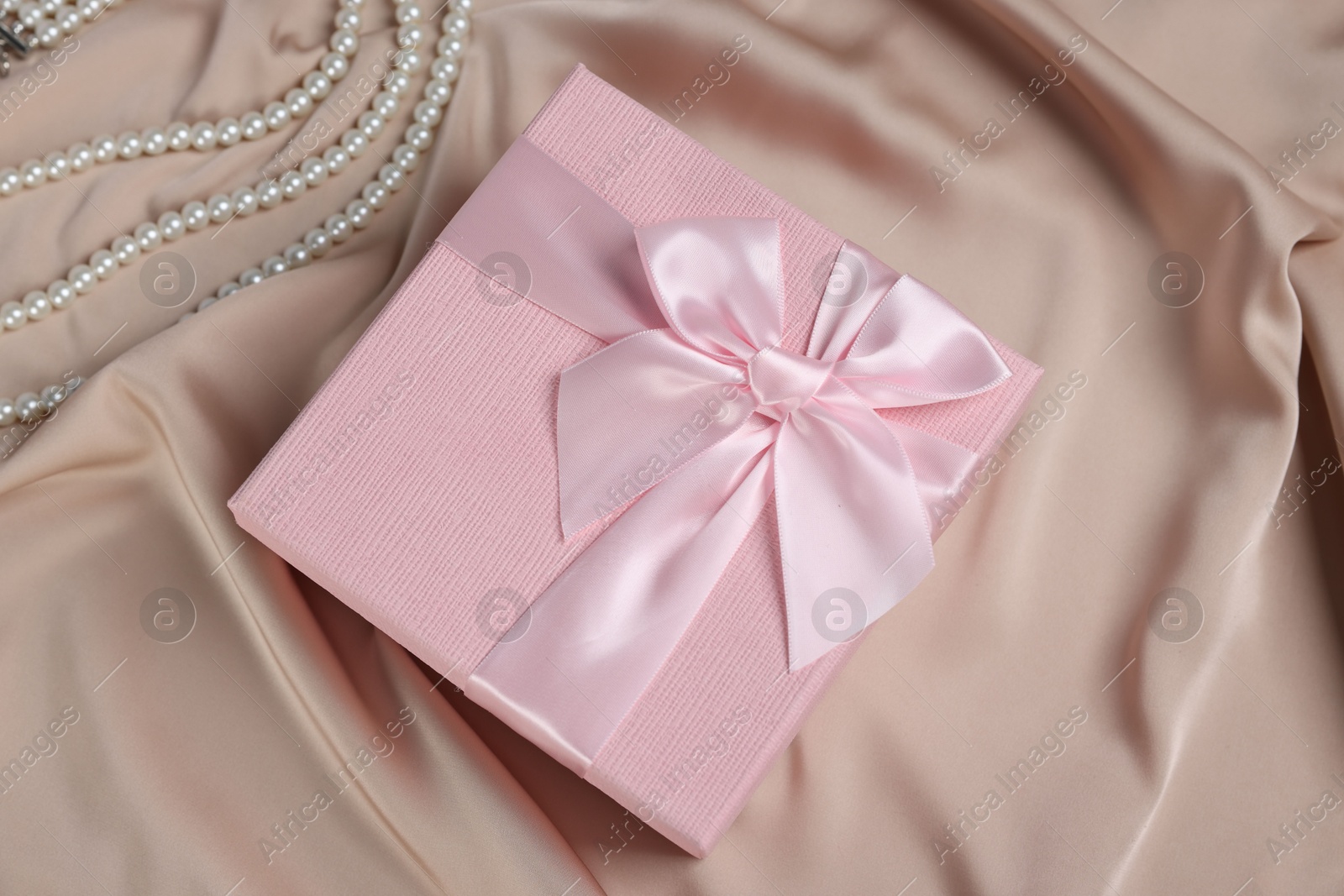 Photo of Gift box for wedding day and pearl necklace on beige fabric, flat lay