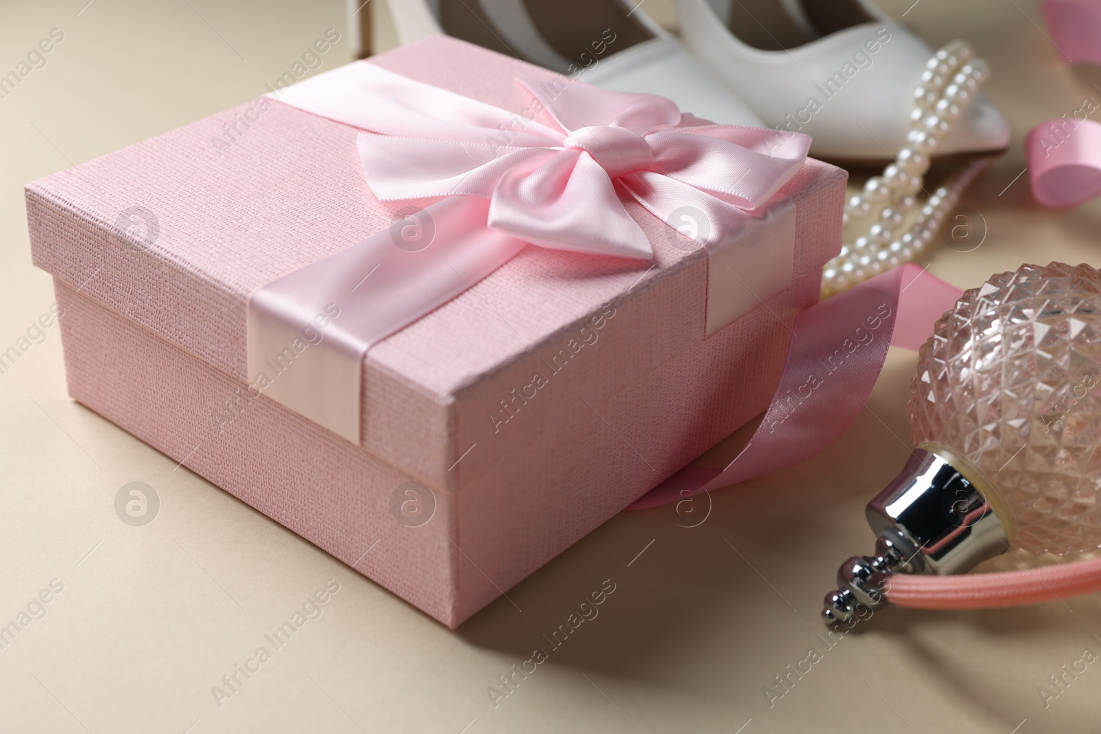 Photo of Gift box for wedding day, perfume bottle, bridal shoes and pearl necklace on beige background, closeup