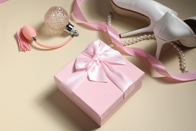 Photo of Gift box for wedding day, bridal shoes, perfume bottle and pearl necklace on beige background, above view