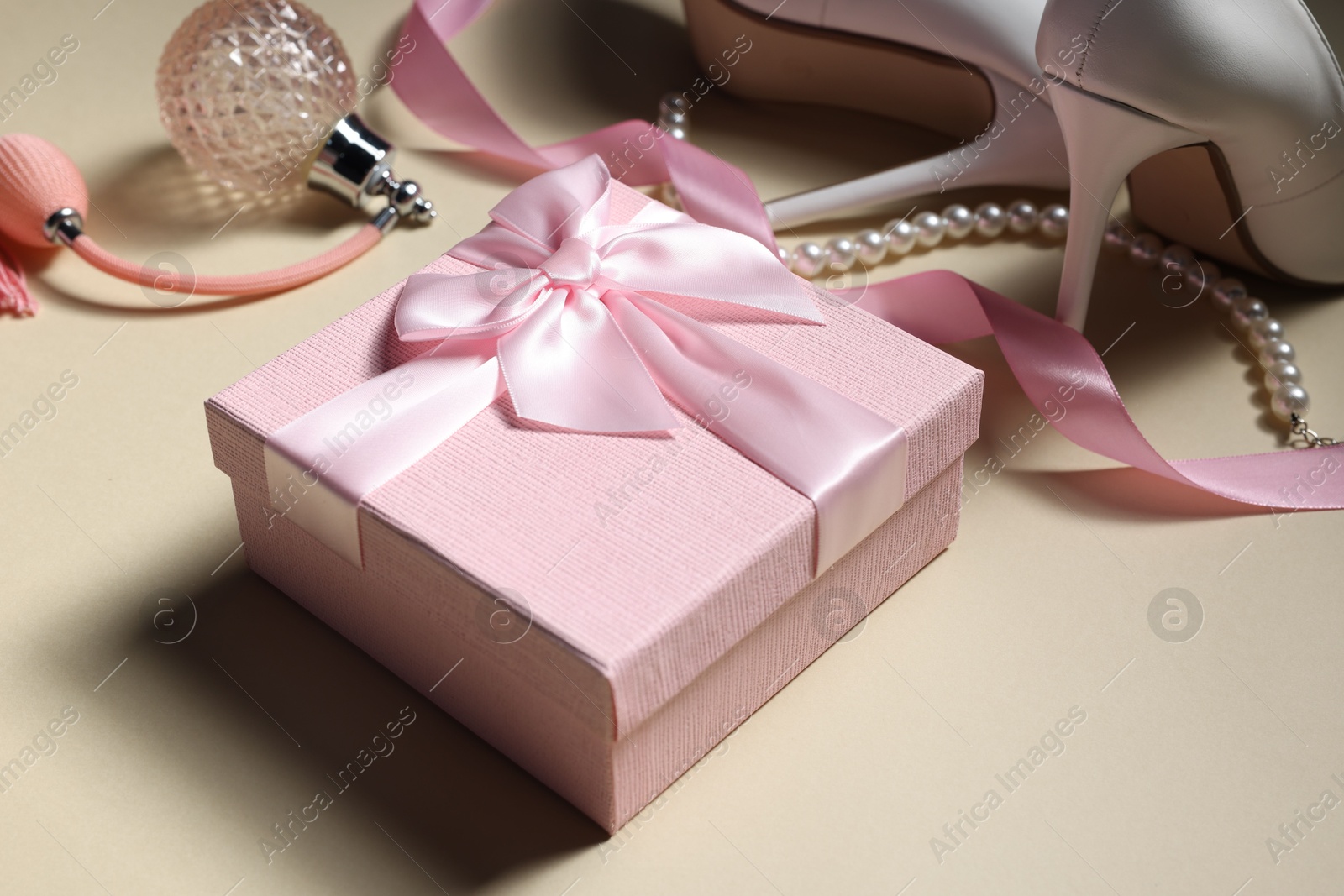 Photo of Gift box for wedding day, bridal shoes, perfume bottle and pearl necklace on beige background, closeup