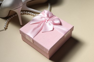 Photo of Gift box for wedding day, bridal shoes, perfume bottle and pearl necklace on beige background, closeup