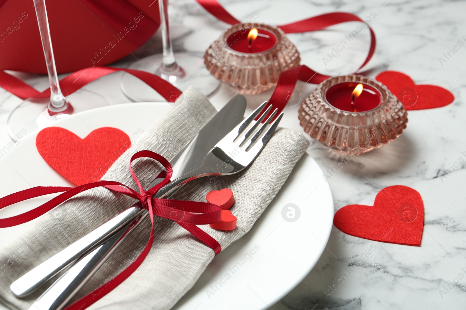 Photo of Romantic place setting for Valentine's day. Plate with cutlery, candles and decorative hearts on white marble table, closeup