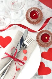 Photo of Romantic place setting for Valentine's day. Plate with cutlery, candles and decorative hearts on white marble table, flat lay