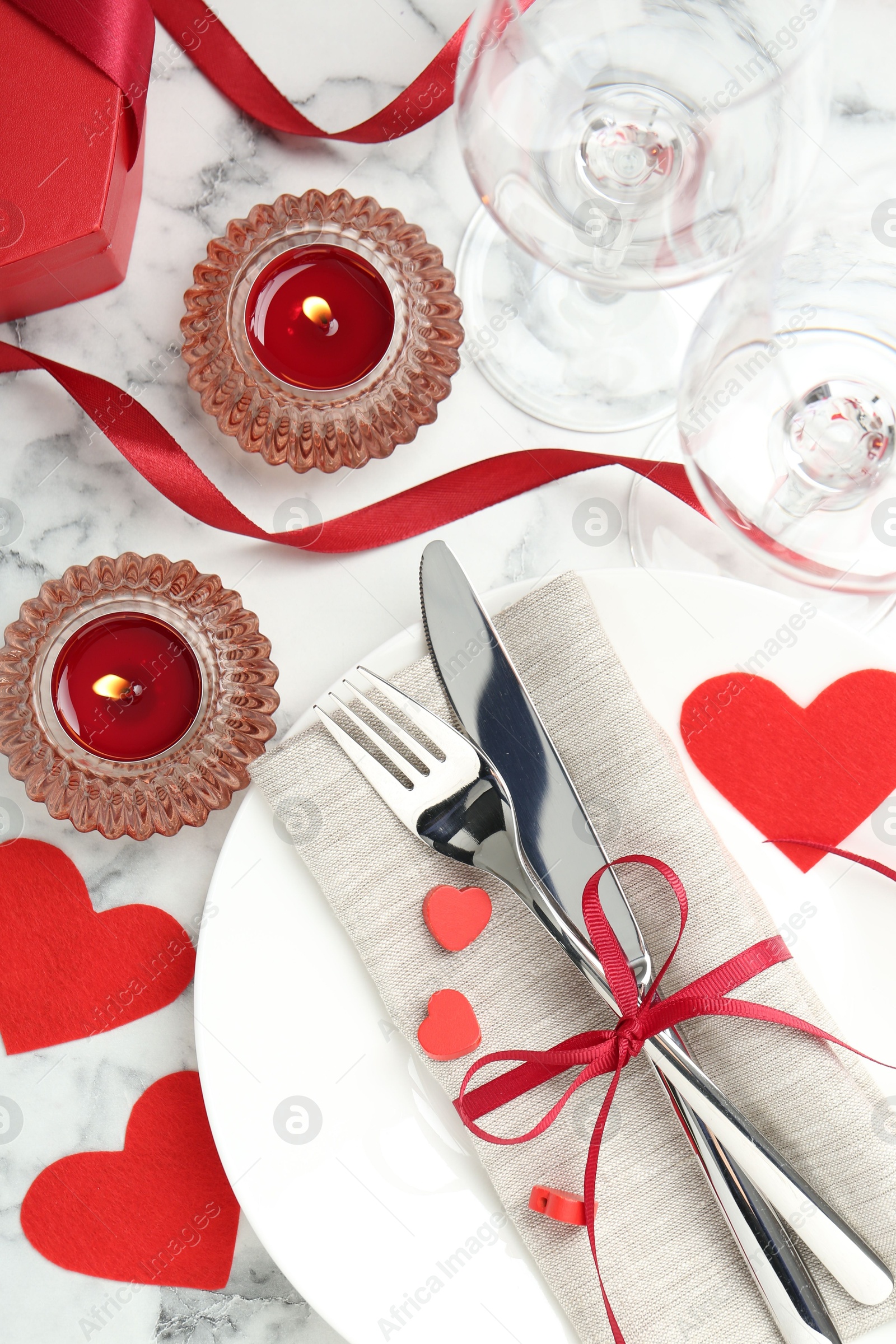 Photo of Romantic place setting for Valentine's day. Plate with cutlery, candles and decorative hearts on white marble table, flat lay