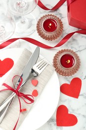 Romantic place setting for Valentine's day. Plate with cutlery, candles and decorative hearts on white marble table, flat lay