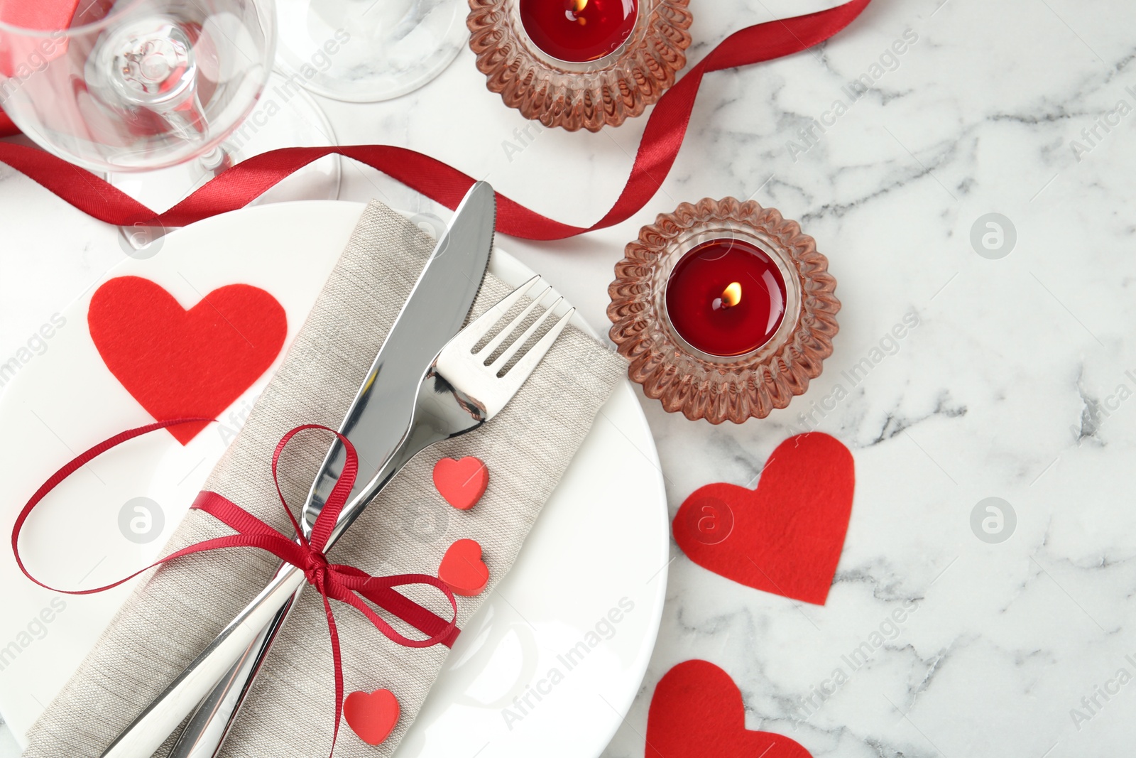 Photo of Romantic place setting for Valentine's day. Plate with cutlery, candles and decorative hearts on white marble table, flat lay