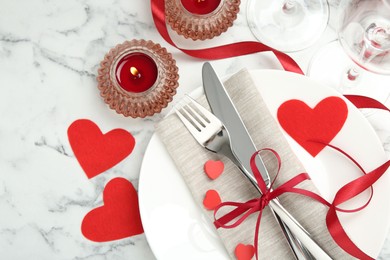 Photo of Romantic place setting for Valentine's day. Plate with cutlery, candles and decorative hearts on white marble table, flat lay