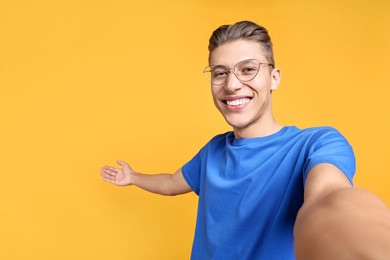 Photo of Happy man taking selfie and welcoming friends or guests on orange background. Space for text