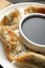 Delicious fried gyoza dumplings with sesame seeds and soy sauce on table, closeup