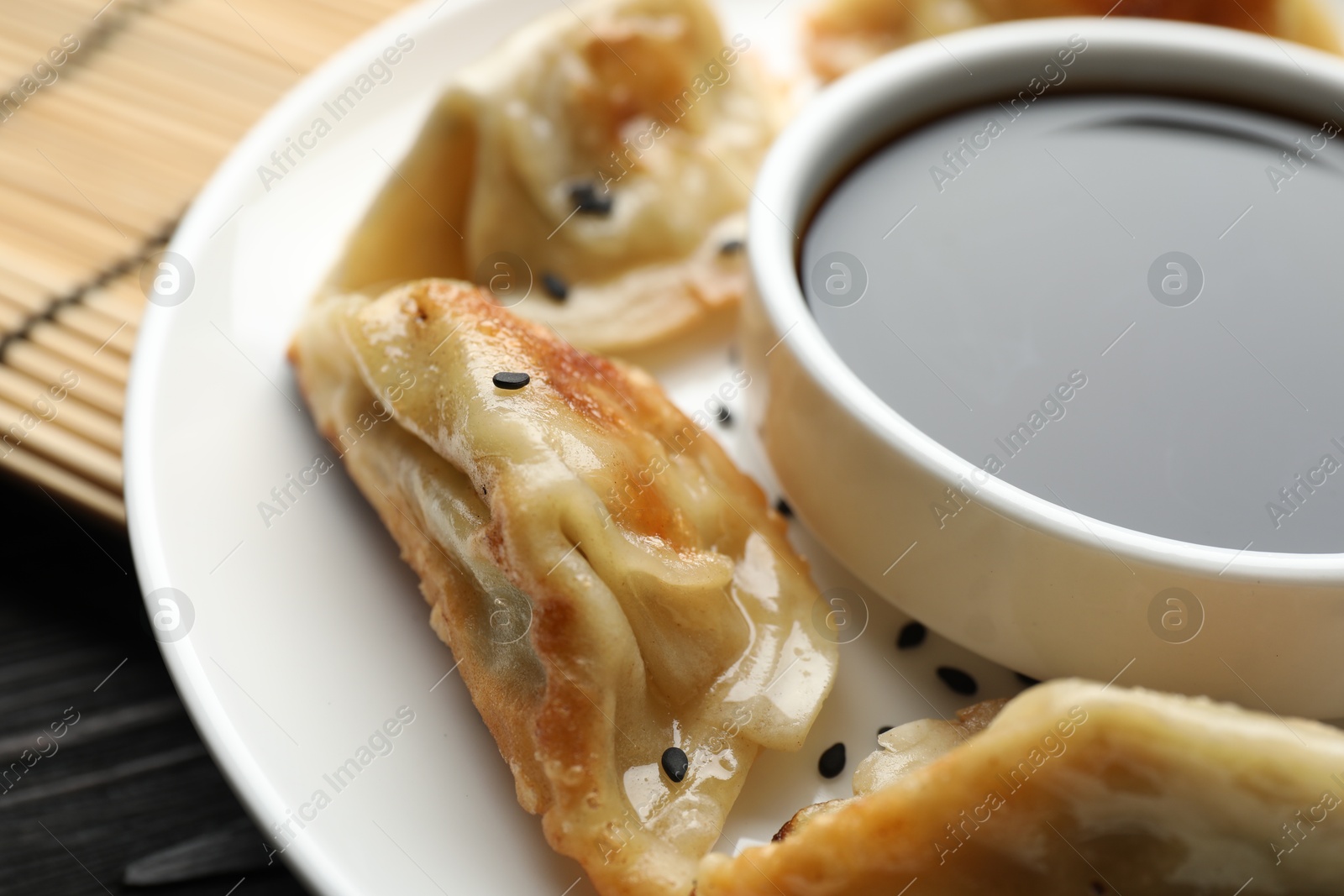 Photo of Delicious fried gyoza dumplings with sesame seeds and soy sauce on table, closeup