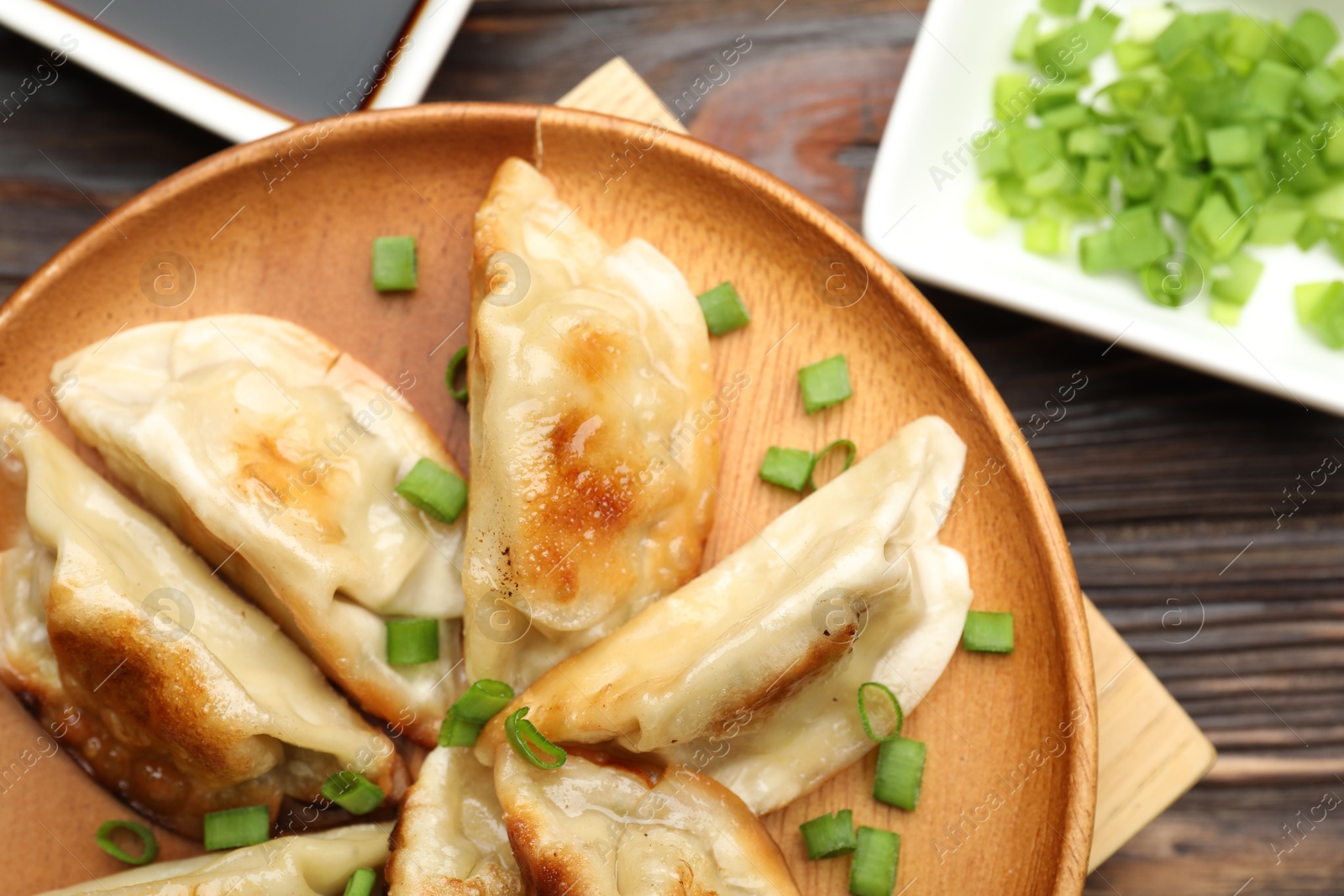 Photo of Delicious fried gyoza dumplings with green onions served on wooden table, top view