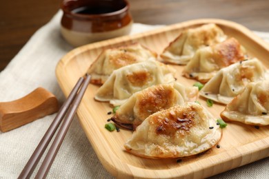 Photo of Delicious fried gyoza dumplings with green onions and soy sauce on table, closeup