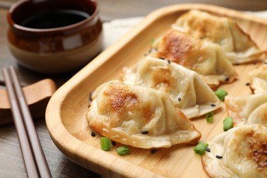 Photo of Delicious fried gyoza dumplings with sesame seeds served on wooden table, closeup