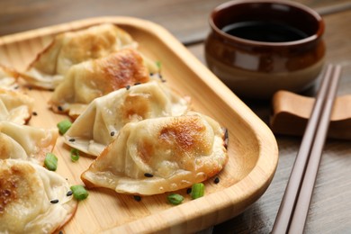 Delicious fried gyoza dumplings with sesame seeds served on wooden table, closeup