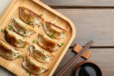 Photo of Delicious fried gyoza dumplings with sesame seeds served on wooden table, flat lay