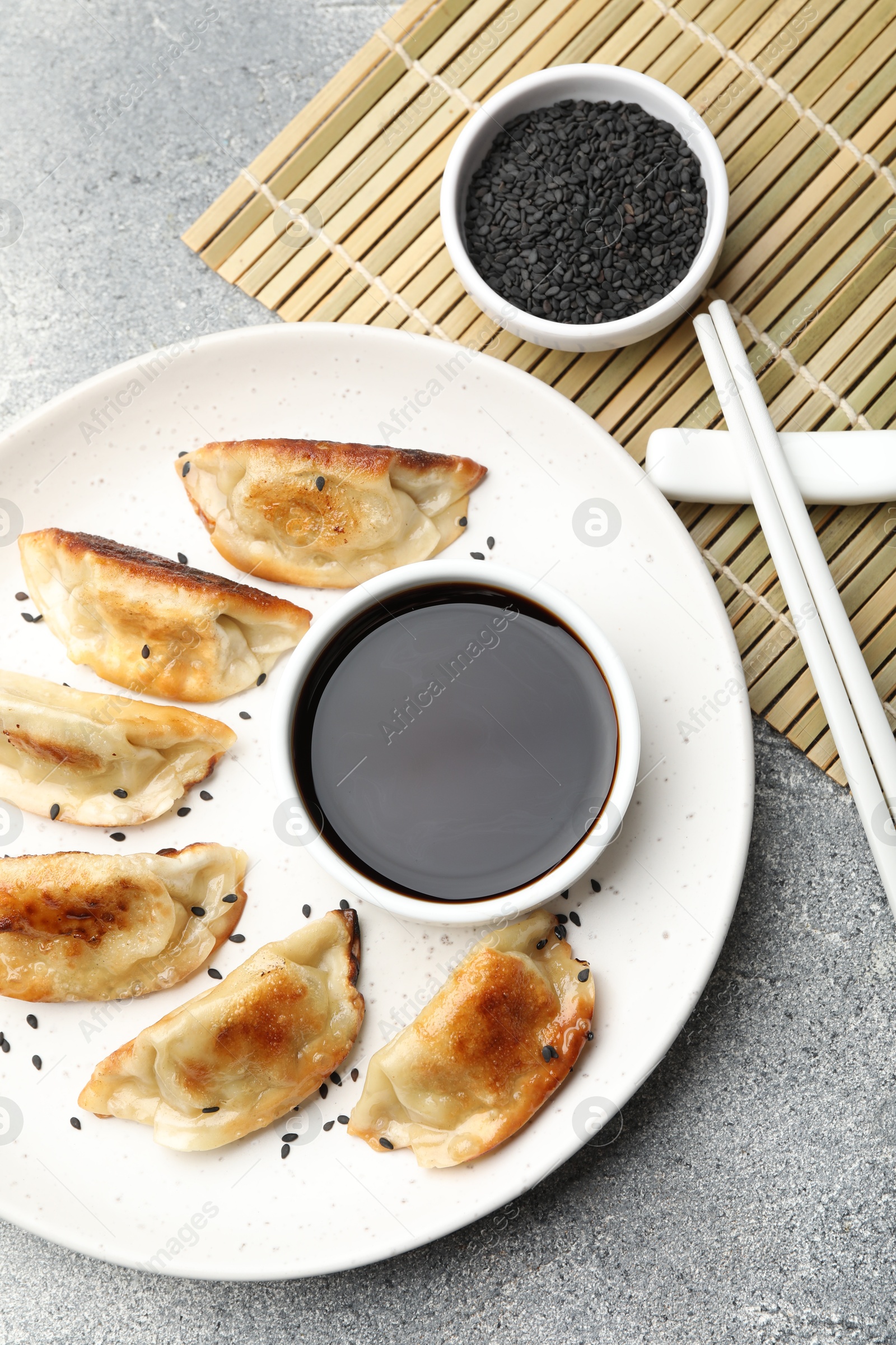 Photo of Delicious fried gyoza dumplings with sesame seeds served on grey table, flat lay