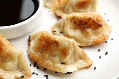 Photo of Fried gyoza dumplings with sesame seeds and soy sauce on table, closeup