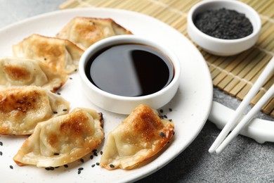 Photo of Delicious fried gyoza dumplings with sesame seeds served on grey table, closeup