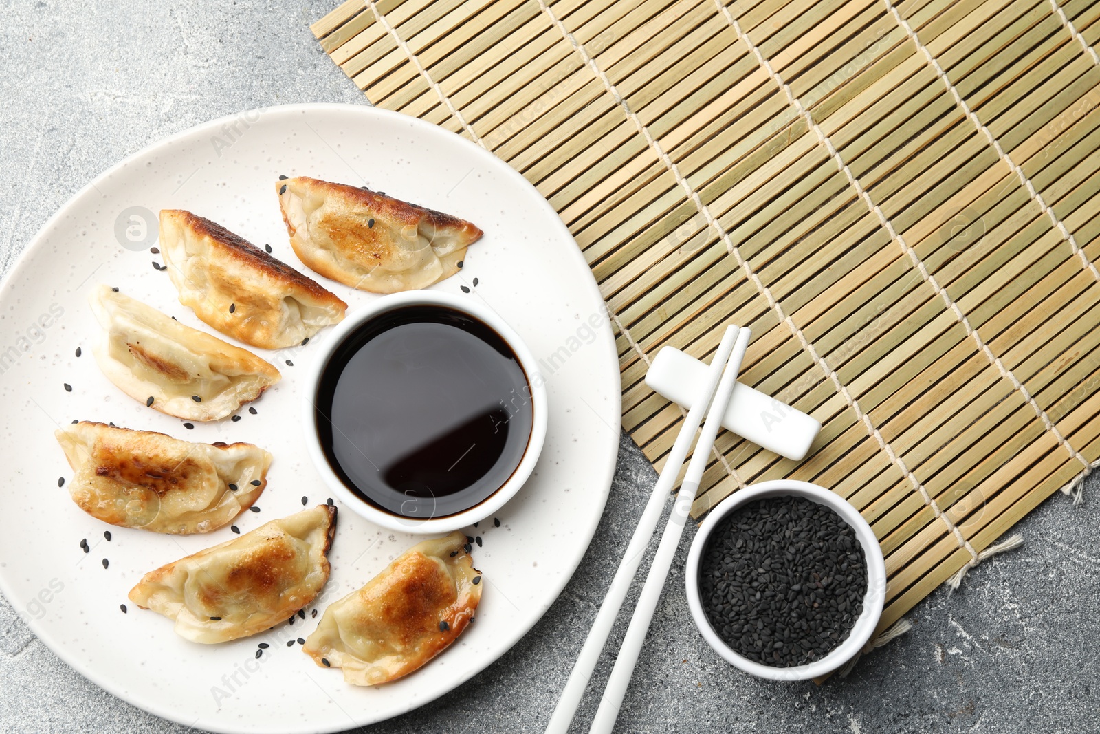 Photo of Delicious fried gyoza dumplings with sesame seeds served on grey table, flat lay