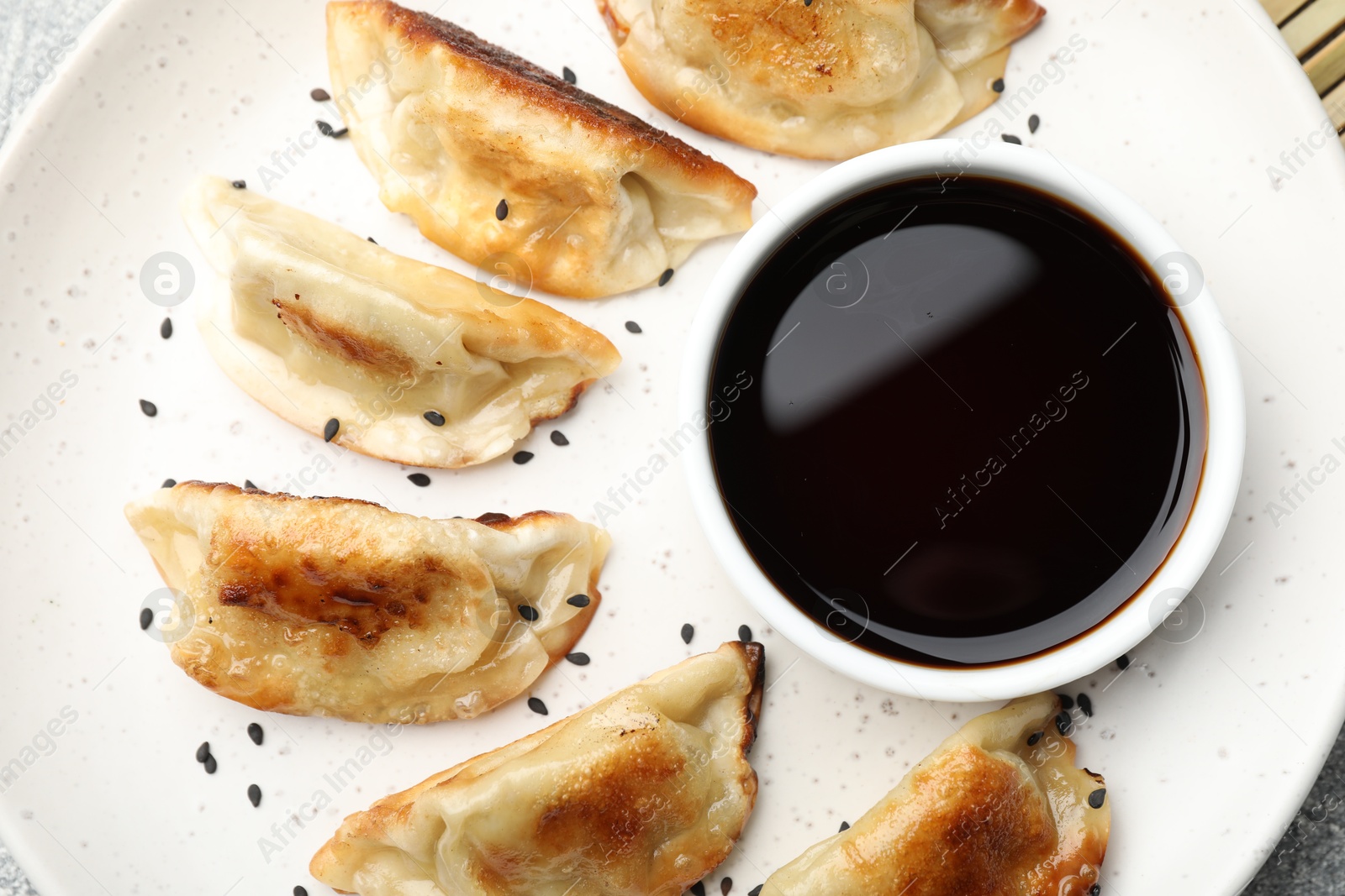 Photo of Fried gyoza dumplings with sesame seeds and soy sauce on table, closeup