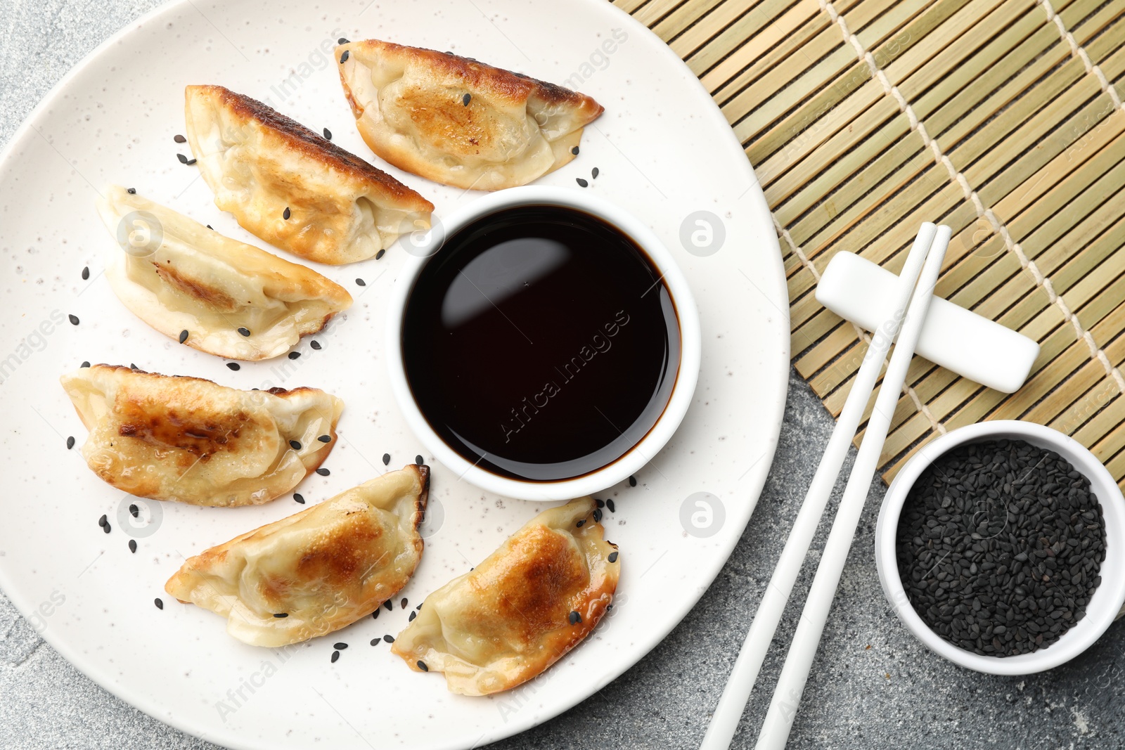 Photo of Delicious fried gyoza dumplings with sesame seeds served on grey table, flat lay