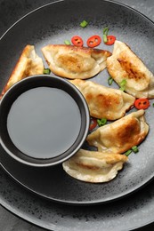 Photo of Fried gyoza dumplings with green onions, chili peppers and soy sauce on black table, top view