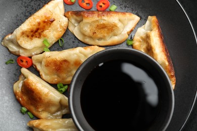 Photo of Fried gyoza dumplings with green onions, chili peppers and soy sauce on black table, top view